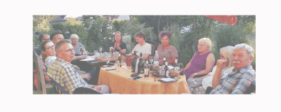 Gruppenfoto der Ortsgruppe. Die Mitglieder sitzen an einem Sommertag am Tisch. Auf dem Tisch stehen u.a. Schreibsachen, Handys, Gläser und Trinkflaschen.